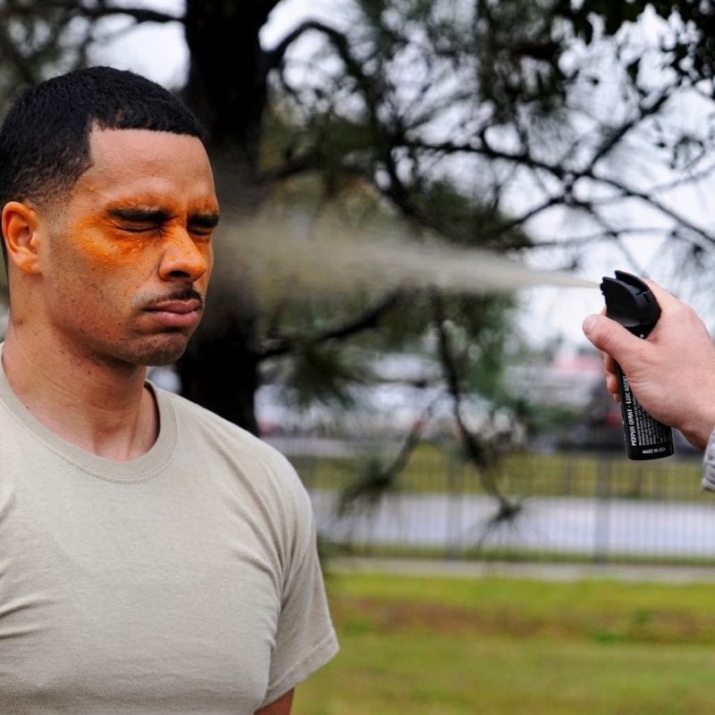 Man with a serious expression using a safety spray canister outdoors.